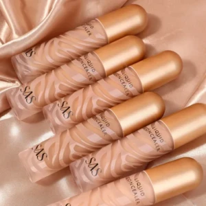 Seis correctores líquidos SAS con diseño de cebra en envase translúcido y tapa dorada sobre tela satinada color melocotón.