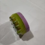 Jabón masajeador en capas verde y morado con semillas, envuelto en plástico.