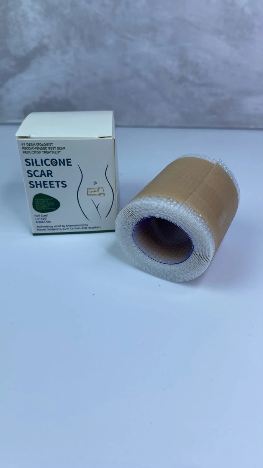 Rollo de cinta de silicona para cicatrizar de 4cm por 1.5m junto a su caja blanca con explicativo sobre su aplicación en zonas quirúrgicas.