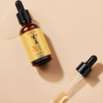Serum de jengibre de 30 ml en frasco de vidrio ámbar con gotero, acompañado de un aplicador separado sobre fondo color crema con gotas de producto.