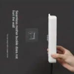 Gancho adhesivo transparente en pared gris, sujetando un aparato blanco vertical, uso sencillo.