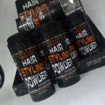 Set de tres envases negros de polvo voluminizador para cabello Mecow, exhibidos en su caja original con etiquetas en naranja y blanco, formato de 5 gramos.