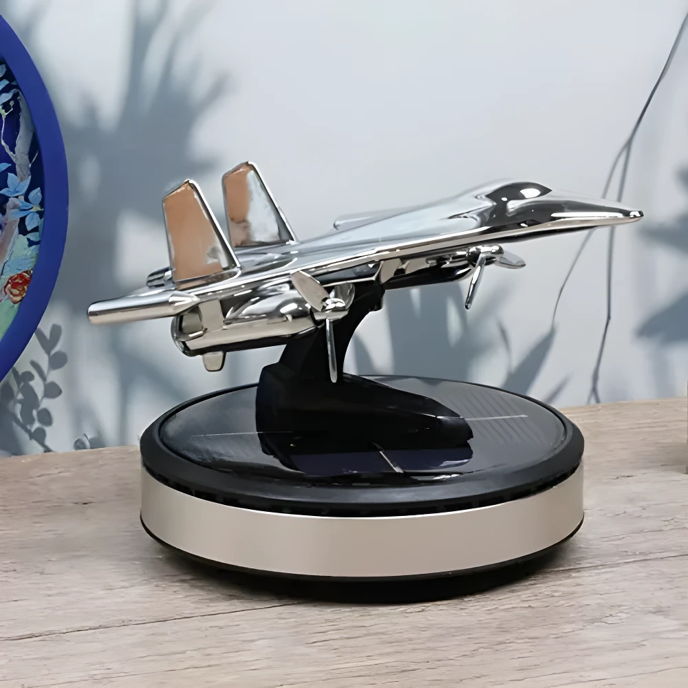 Ambientador solar para carro con diseño de avión plateado y detalles en cobre, sobre base giratoria con panel solar.