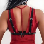 Arnés gótico de cuero negro regulable sobre vestido rojo, detalle de hebillas metálicas en la espalda.