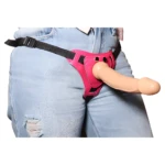 Arnés erótico rosa ajustable con falo de silicona, sobre jeans rasgados.