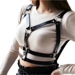Arnés de cuerpo de cuero negro con tiras y aros, sobre blusa beige acanalada.