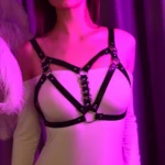 Arnés de cuero negro para mujer, con tiras cruzadas y anillos metálicos, para uso sobre ropa.