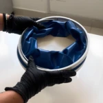 Balde plegable azul con borde blanco sujetado por manos enguantadas.