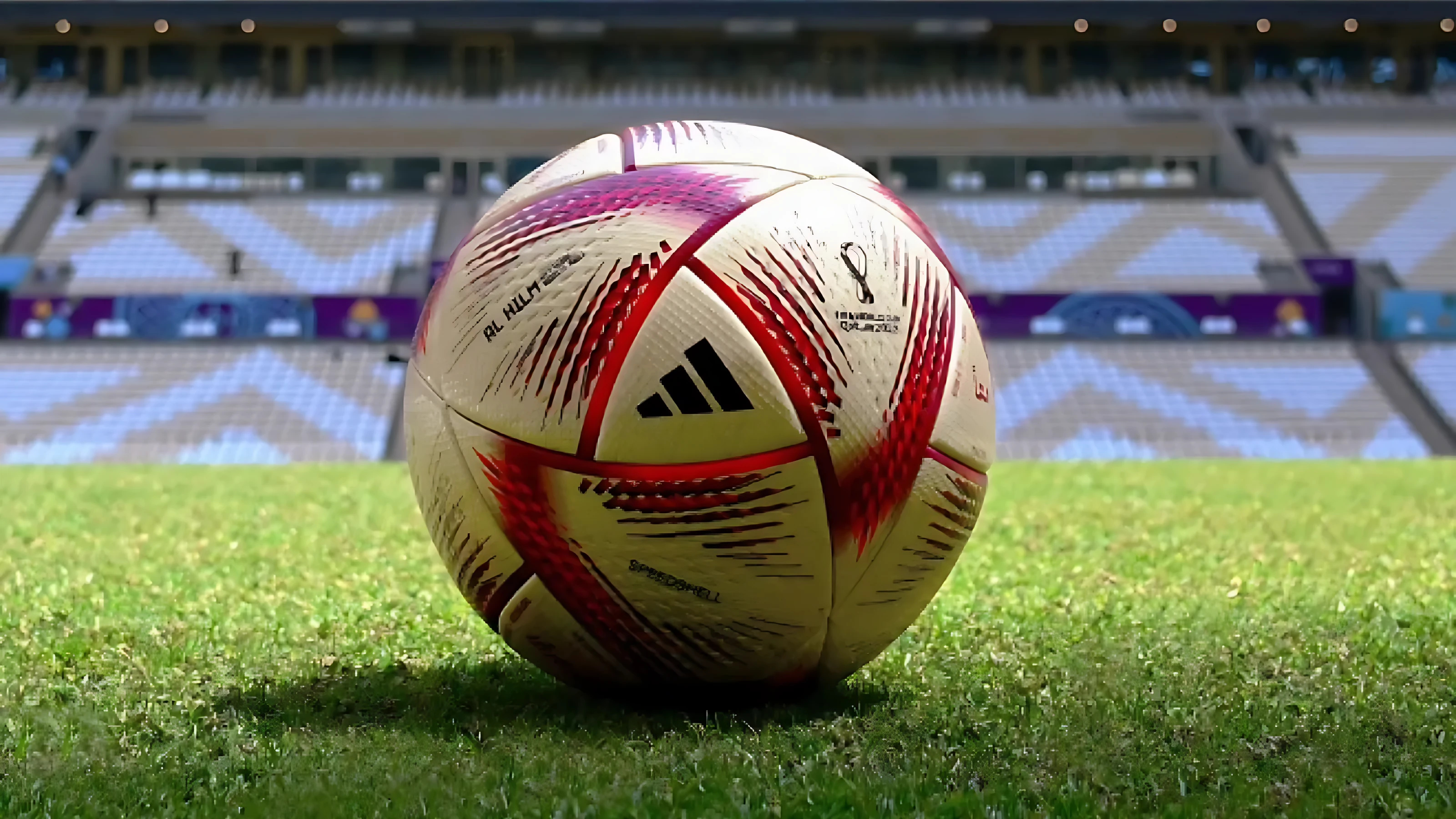 Balón de fútbol profesional Adidas Al Rihla #5 sin costuras, blanco con detalles rojos, sobre césped de estadio.