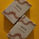 Barra exfoliante aclarante Epoch con barro marino, 100g. Envase blanco con diseño de rayos y puntos sobre fondo amarillo.