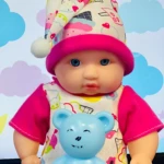 Bebé muñeco con pijama estampado de nubes y corazón, gorro de dormir con pompón, y osito azul de plástico con letra N.