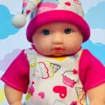 Muñeco bebé con pijama blanco y estampado de dulces, gorro rosa, ojos azules, fondo de nubes.