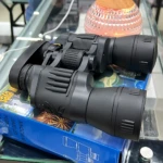 Binoculares negros 20x50 con prismas Bak-4, sobre caja azul con diseño de fuegos artificiales y texto "BINOCULAR".