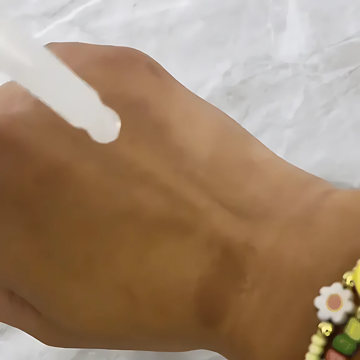 Suero coreano Bio Rice Serum 30ml aplicándose sobre piel clara, con pulsera de abalorios florales.