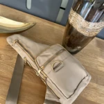 Bolso bandolera impermeable color beige, con cremalleras doradas y correa ajustable, ideal para llevar lo esencial.