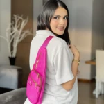 Bolso bandolera impermeable Spice fucsia con cremalleras doradas, usado por mujer en ambiente interior.