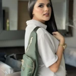 Mujer con bolso bandolera Spice verde, impermeable, diseño moderno con cremalleras doradas.