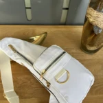 Bolso bandolera blanco impermeable con cremalleras doradas y asa ajustable, perfecto para uso diario.