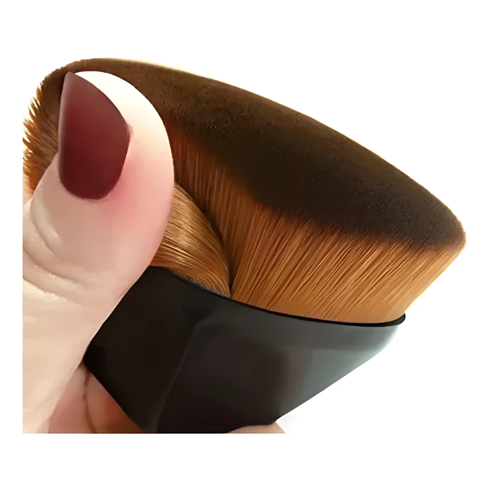Brocha mágica de maquillaje negra, cerdas suaves y densas color café para aplicar base, sostenida por mano con uña color vino.