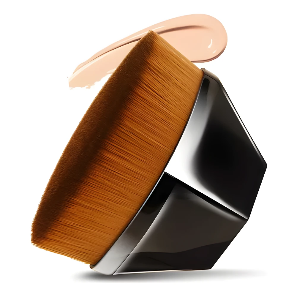 Brocha mágica para base de maquillaje con cerdas densas color miel y mango negro facetado, con una gota de base cremosa encima.