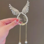 Broche para cabello circular con perlas, alas laterales de encaje brillante y dos cadenas colgantes con dijes de perla en los extremos.