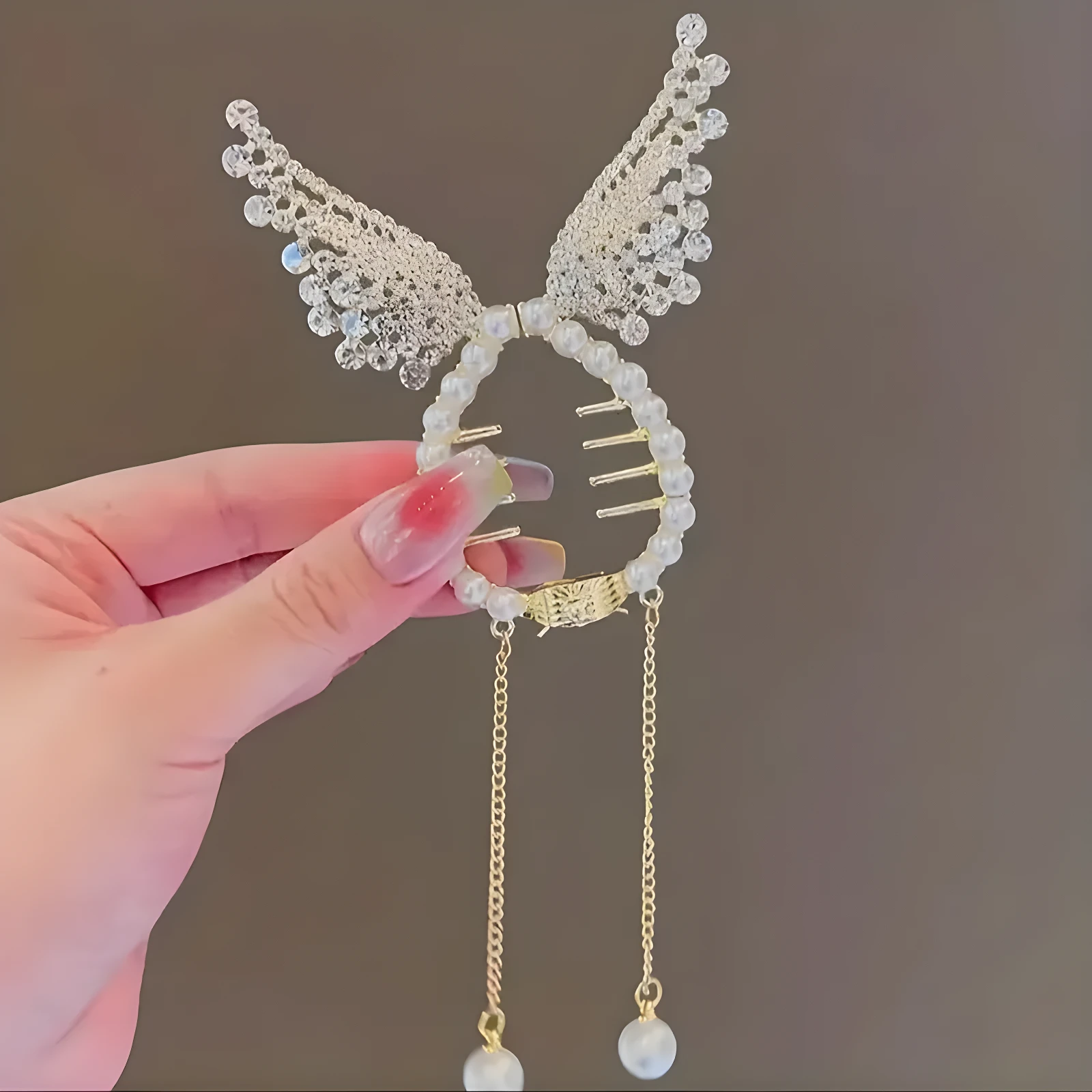 Broche para cabello circular con perlas, alas laterales de encaje brillante y dos cadenas colgantes con dijes de perla en los extremos.