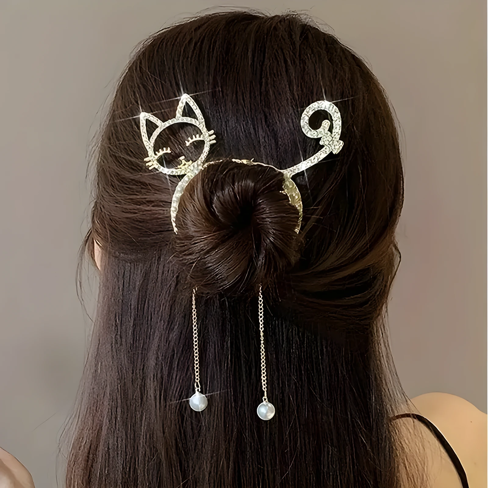 Peinado de moño con pinza metálica dorada de diseño felino, decorada con una silueta de gato y cola rizada, que incluye dos delicados dijes con perlas.