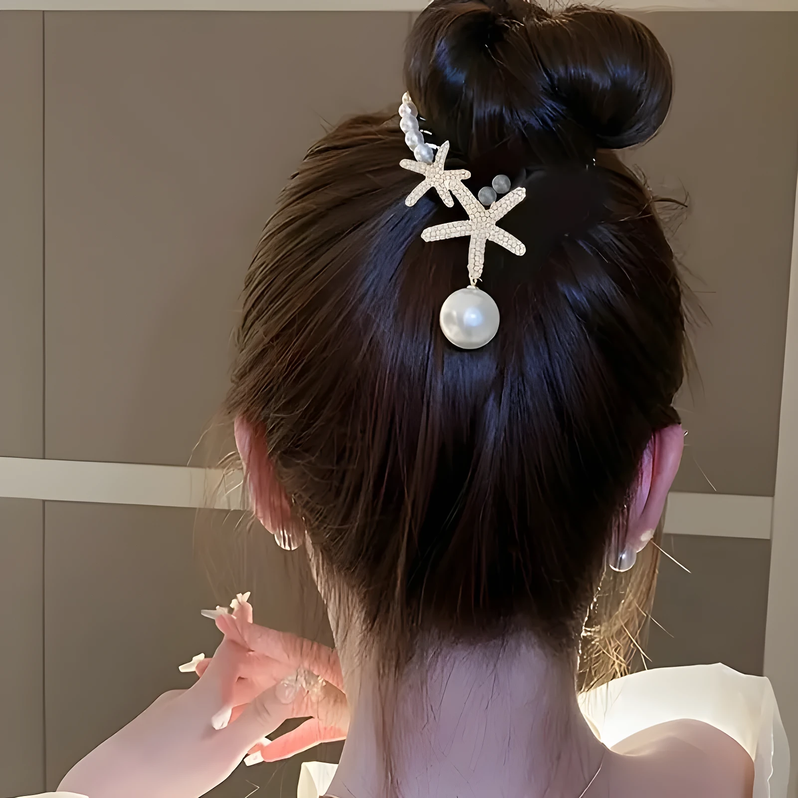 Broche para cabello tipo pinza con diseño de dos estrellas de mar plateadas y perlas decorativas, aplicado en un recogido elegante de tono castaño oscuro.