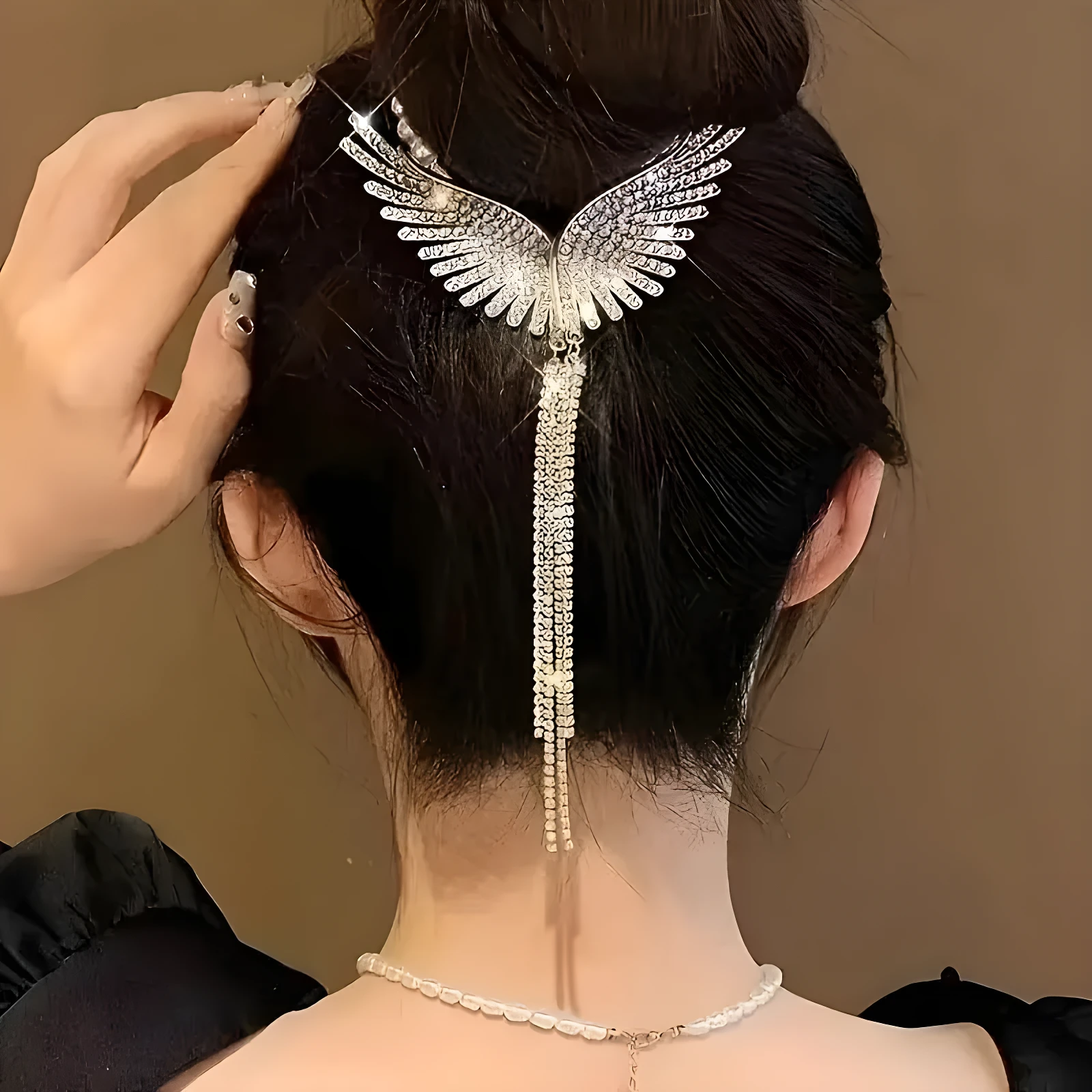 Pinza para cabello color plata con diseño de alas detalladas y flecos de pedrería colgantes, aplicada sobre un peinado recogido en tono oscuro.