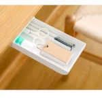 Cajón blanco adhesivo compacto para escritorio con tijeras, bolígrafo y mini libreta sobre superficie de madera.