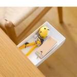 Cajón blanco adhesivo para escritorio con llavero amarillo, tarjetas de papel y silla de mimbre al fondo.