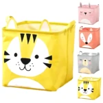 Canasta organizadora amarilla plegable con diseño de tigre, ideal para juguetes. Variantes en rosa, naranja y gris se ven al fondo.