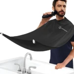 Capa negra impermeable para corte de barba, con ventosas, capturando recortes y un hombre afeitándose.