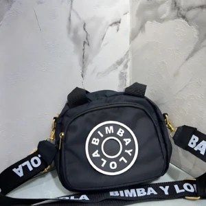 Carriel Bimba y Lola negro con logo circular blanco, correa estampada, ideal para llevar lo esencial.