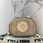 Carriel cruzado Bimba y Lola color beige con logo circular y correa con inscripción de la marca.