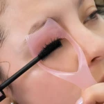Cepillo rosa para pestañas y cejas con aplicador de máscara, usado por persona con piel clara.