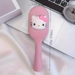 Cepillo compacto color rosa con relieve de Hello Kitty, mide 5.5 cm de ancho por 17 cm de largo, sobre superficie blanca junto a un reloj y teclado.