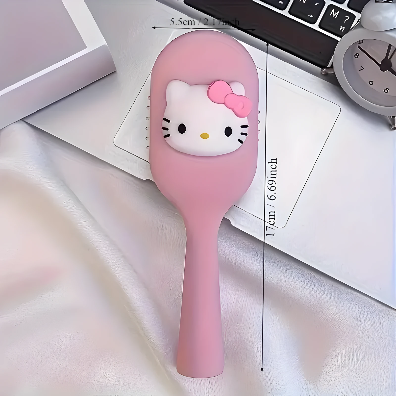 Cepillo compacto color rosa con relieve de Hello Kitty, mide 5.5 cm de ancho por 17 cm de largo, sobre superficie blanca junto a un reloj y teclado.