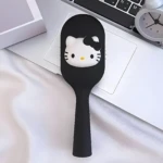 Cepillo para el cabello color negro con aplique decorativo de Hello Kitty, diseño compacto y ergonómico sobre superficie blanca junto a un teclado.