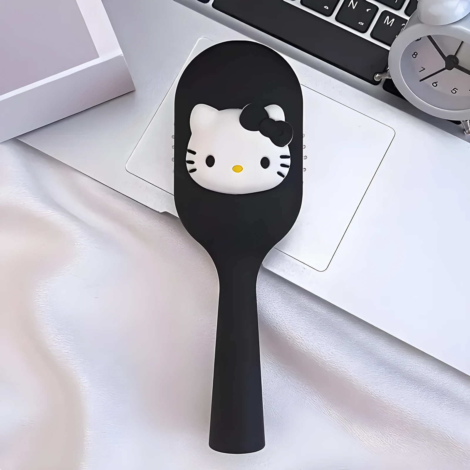 Cepillo para el cabello color negro con aplique decorativo de Hello Kitty, diseño compacto y ergonómico sobre superficie blanca junto a un teclado.