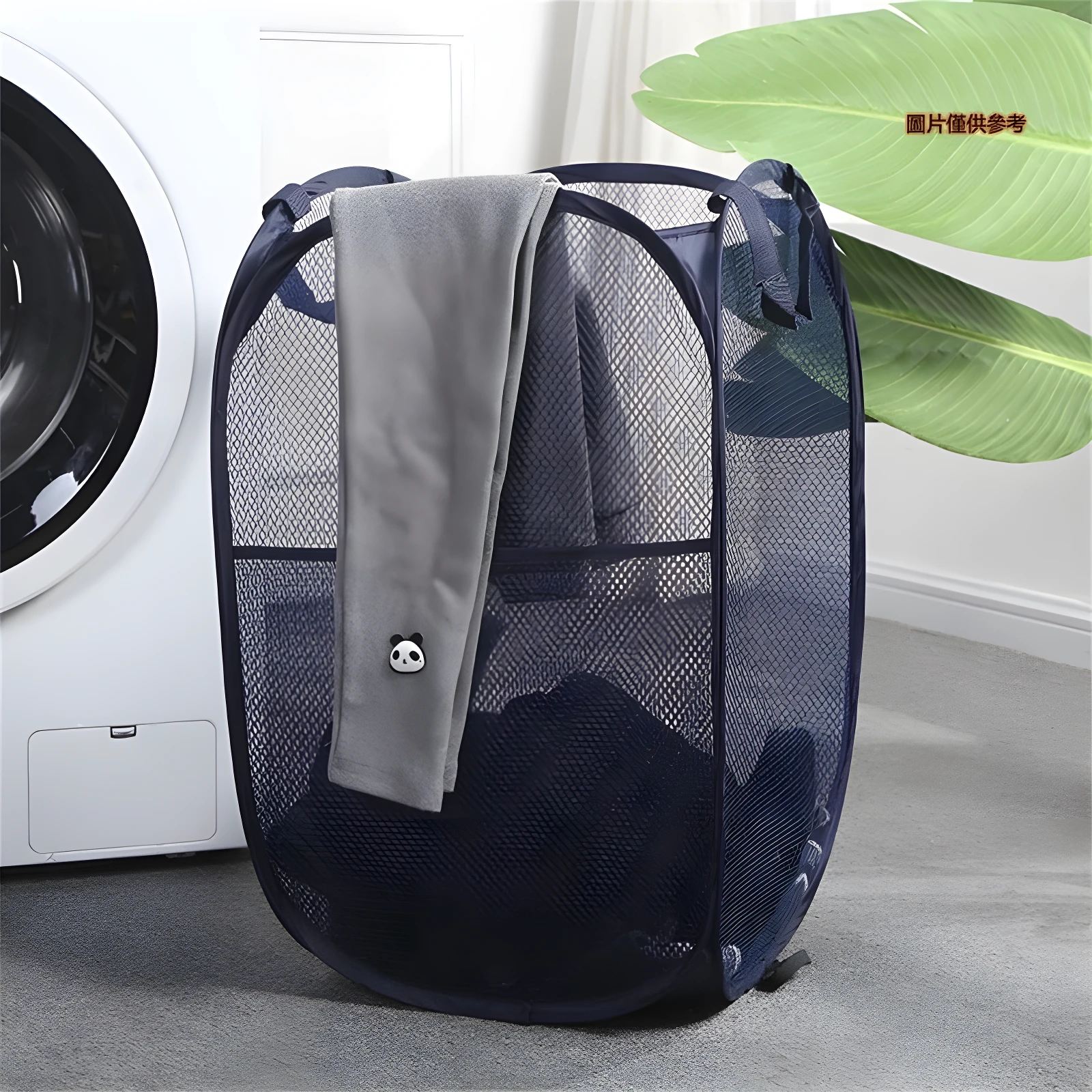 Cesta plegable de malla azul marino para ropa sucia, junto a lavadora, con toalla gris y adorno de panda.