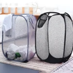 Cestas plegables de malla para ropa: una gris con ropa y otra negra vacía en una habitación.