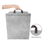 Cesto de ropa colgante plegable plateado, textura aislante térmica, con mango resistente sujetado por mano.