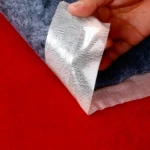 Cinta doble faz transparente multiuso desplegándose de alfombra gris sobre fondo rojo.