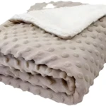 Cobija térmica suave color beige con textura de puntos y borde de almohada blanca.