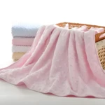 Cobija térmica rosa con textura de corazones, junto a almohada y cobijas apiladas en canasta de mimbre.