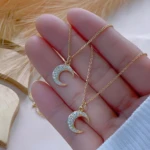 Set x2 collares de oro para mujer con colgante de luna creciente adornado con brillantes, sostenidos en mano.