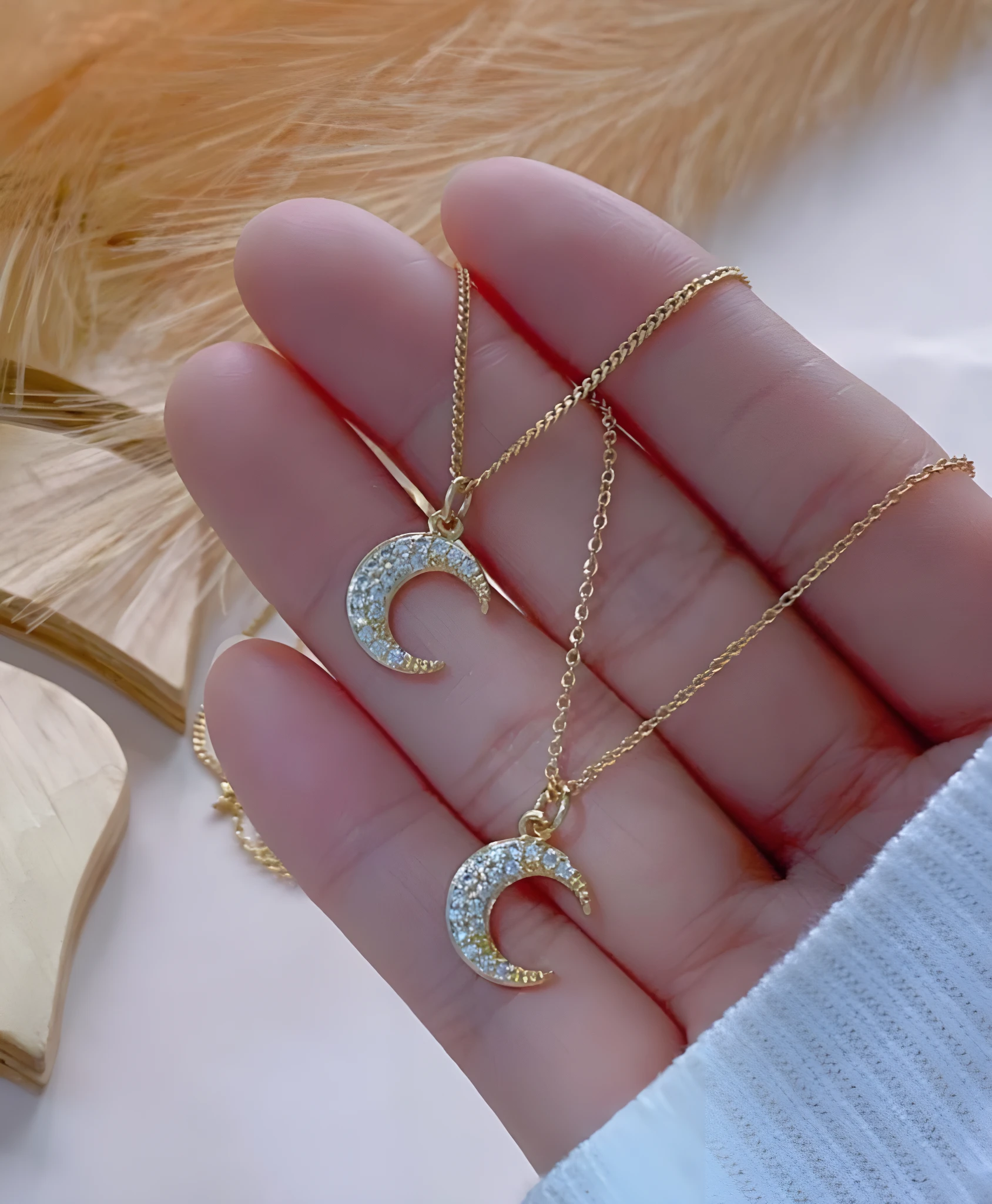 Set x2 collares de oro para mujer con colgante de luna creciente adornado con brillantes, sostenidos en mano.