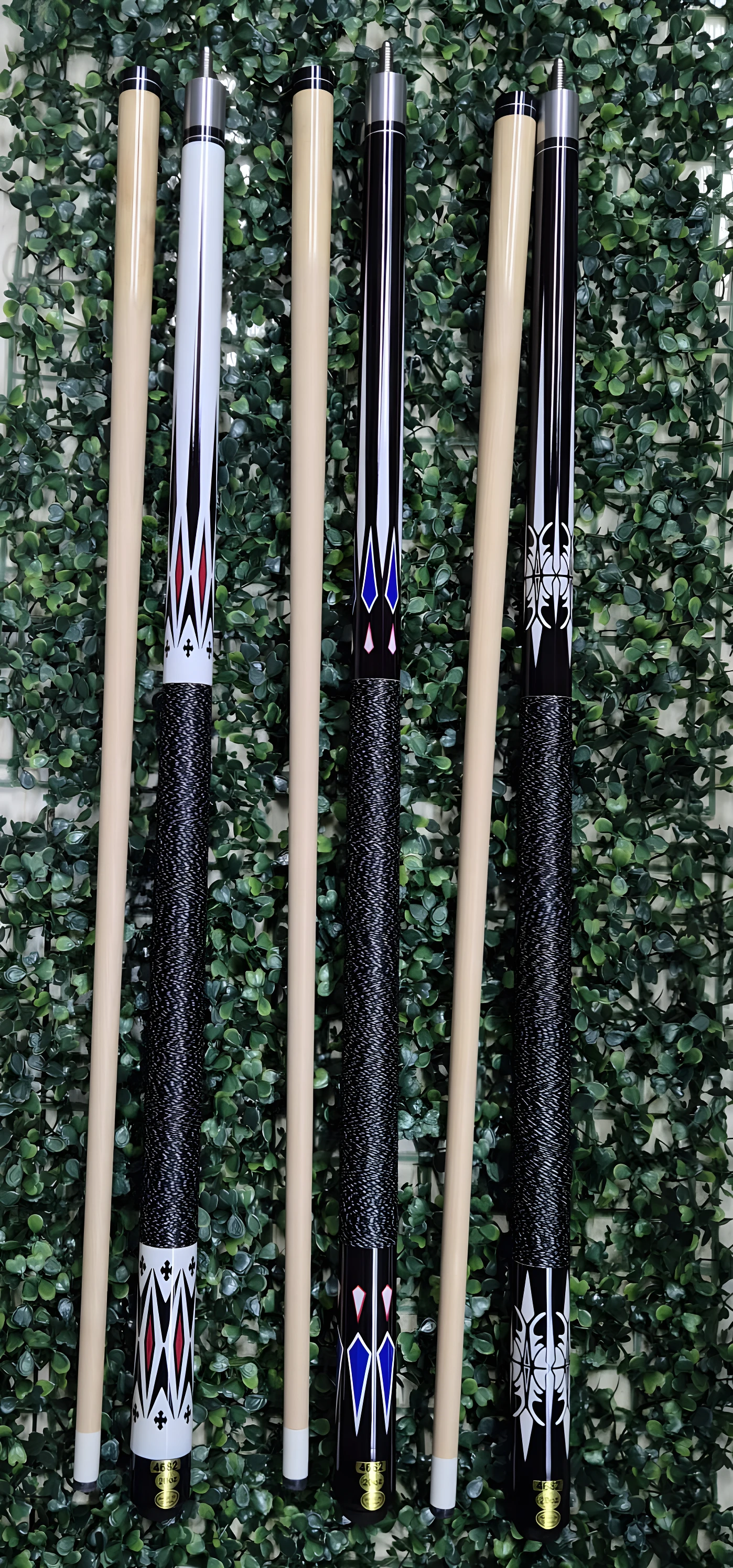 Tacos de billar con diseños variados y envoltura negra, sobre fondo de hojas verdes.