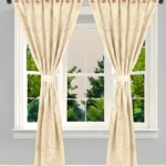 Cortina Jacquard beige con diseño de círculos y diamantes, atada a los lados, en ventana doble con vista a árboles.